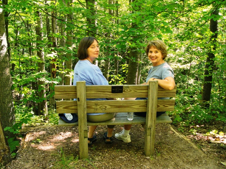 two woman sitting on a bench next to each other in the woods