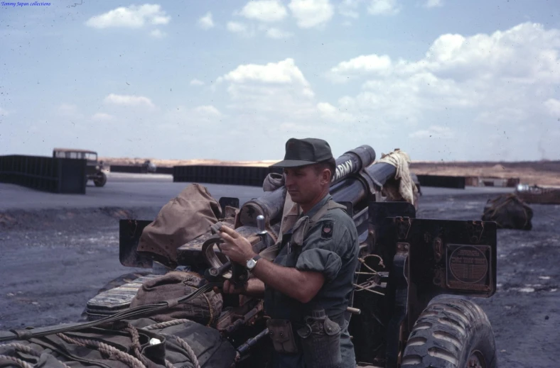 a man stands next to an army truck holding a pack