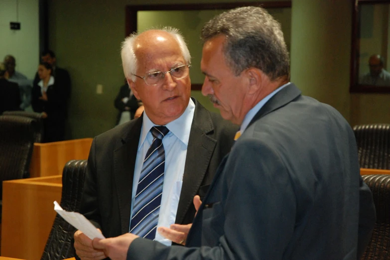 two men are speaking in an empty conference room