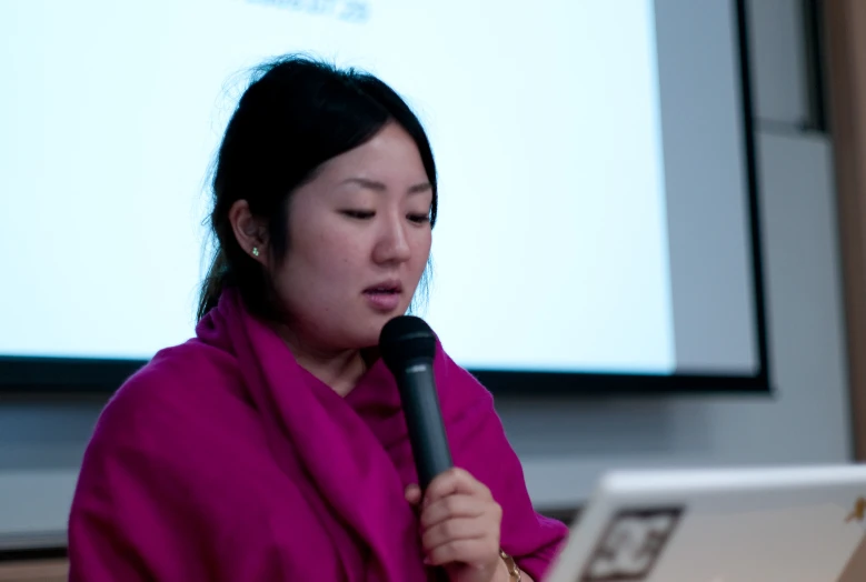 a woman holding a microphone and speaking on the screen