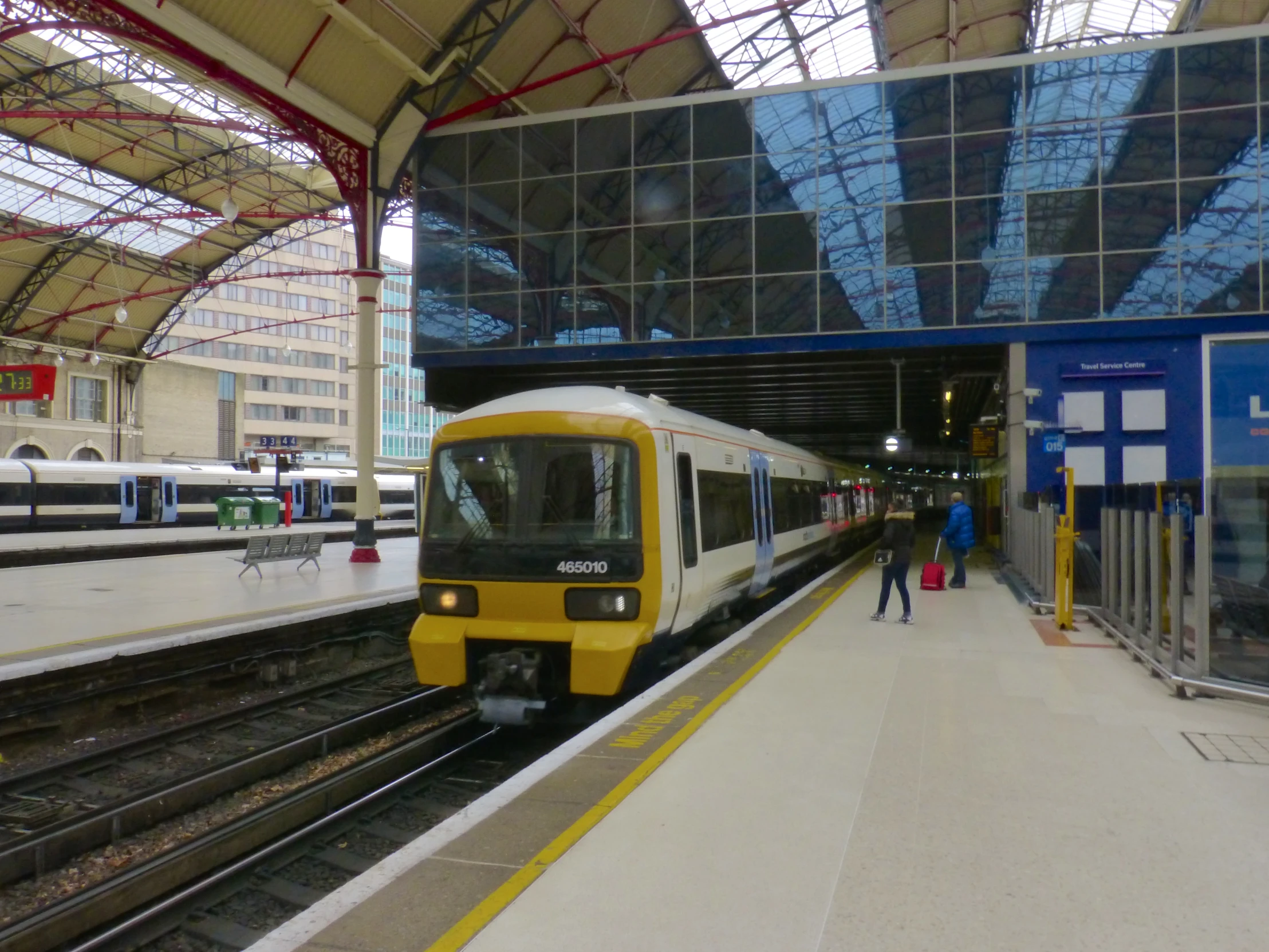 two trains stopped at a train station, the one in yellow is pulling up to the platform