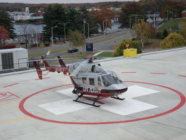 a small helicopter on an airport tarmac with trees and buildings in the background