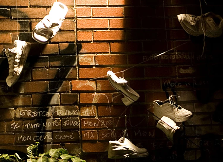 multiple shoes hang on brick wall with spray paint writing