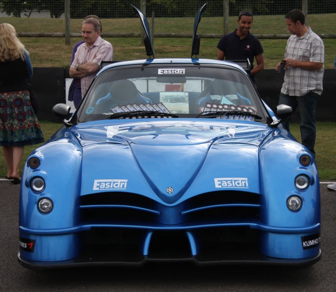 people looking at blue car with surfboards on top