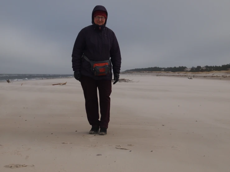 a man on the beach wearing black and holding ski poles