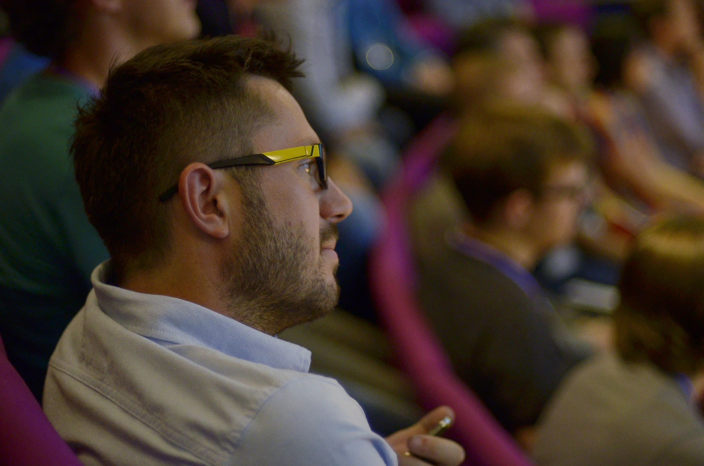 man in glasses sitting in front of crowd of people