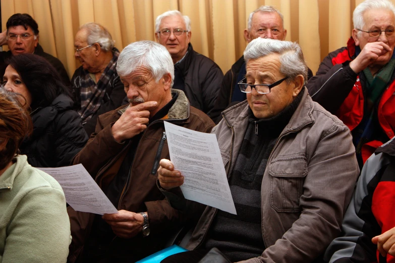 many people in jackets sitting and looking at a sheet