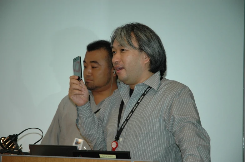 two men at a podium take pos with their cell phones