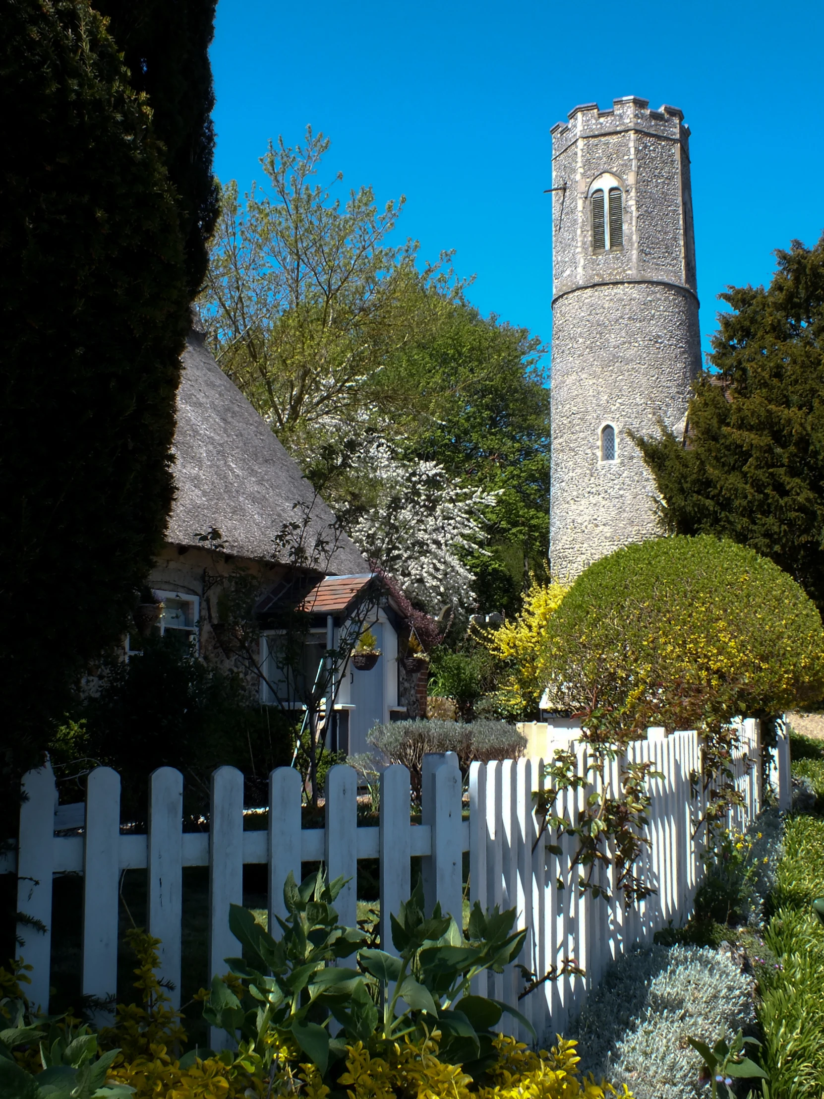 a garden next to a white picket fence in front of a stone church