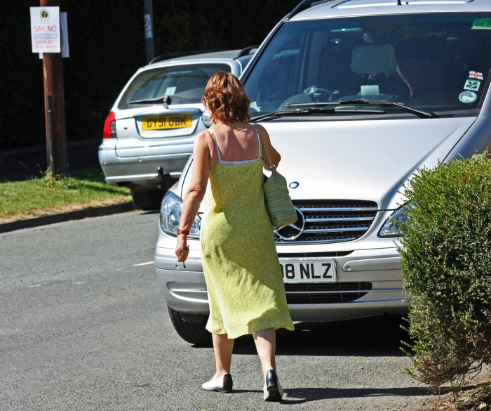 a woman in yellow dress walking past cars