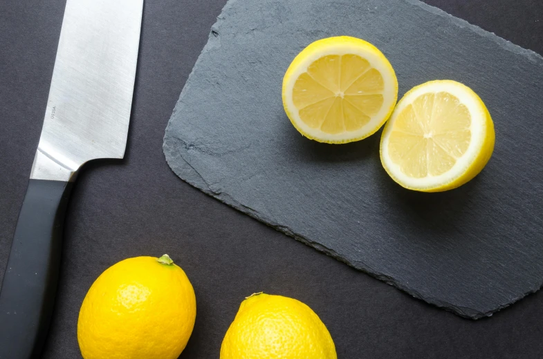 a knife sitting on top of a cutting board next to lemons, inspired by Grillo Demo, trending on unsplash, slate, background image, limestone, taken from the high street