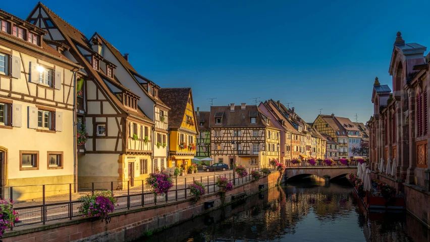 a river running through a city next to tall buildings, by Juergen von Huendeberg, pexels contest winner, renaissance, french village exterior, beams of golden light, pink, 4k image”