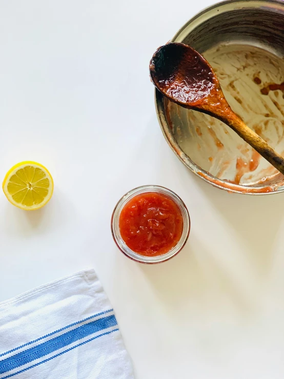 a white table topped with a bowl of sauce and a wooden spoon, by Maggie Hamilton, unsplash, process art, holding hot sauce, lemon, dwell, instagram story