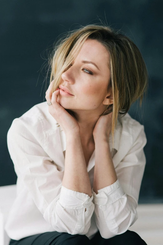 a woman sitting on top of a white chair, a portrait, trending on unsplash, wearing a linen shirt, sydney sweeney, thoughtful pose, camilla luddington