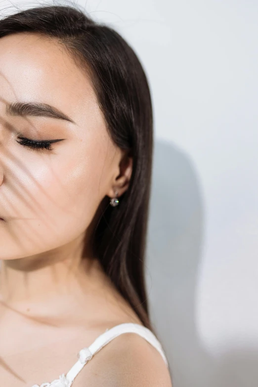 a woman standing in front of a white wall with her eyes closed, inspired by Qian Xuan, trending on unsplash, light and space, earring, exhausted face close up, square jaw-line, directional sunlight skewed shot