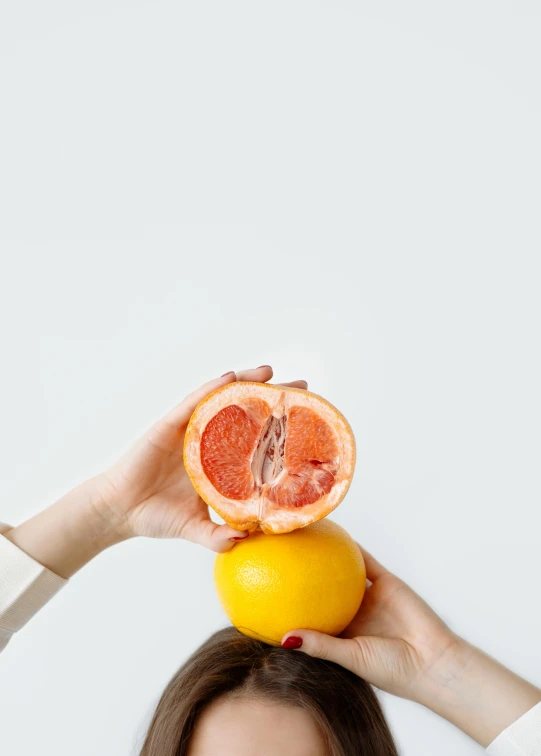 a woman holding a grapefruit on top of her head, by Carey Morris, trending on unsplash, plain background, woman holding another woman, anatomy, yellow-orange