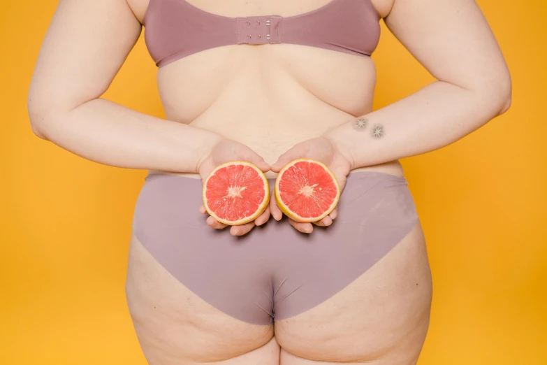 a woman holding two slices of grapefruit in her hands, inspired by Fernando Botero, trending on pexels, figuration libre, hips, steroids, coloured photo