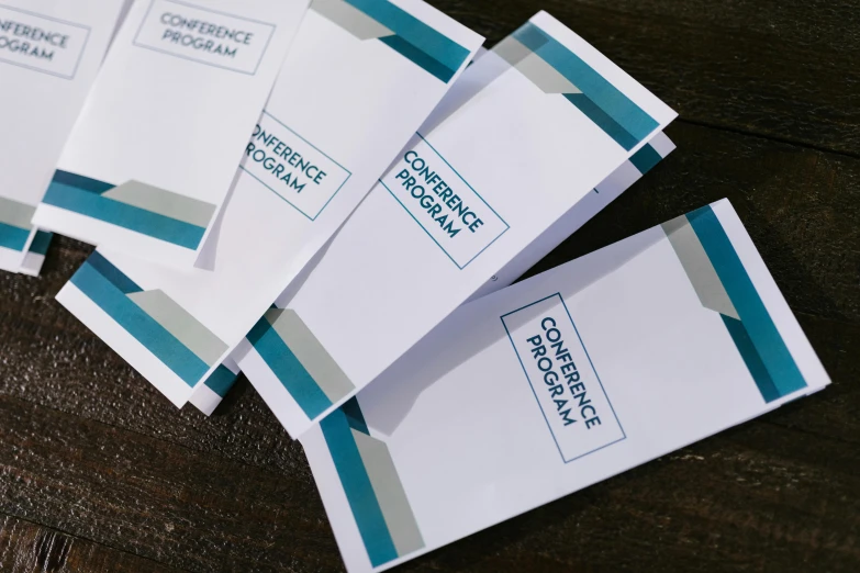 a pile of business cards sitting on top of a wooden table, private press, white and teal metallic accents, brochure, performance, in a row