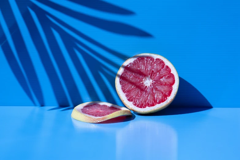 a grapefruit cut in half on a blue surface, by Nathalie Rattner, pexels contest winner, photorealism, pink sunlight, jungle fruit, 🦩🪐🐞👩🏻🦳, gradient and patterns wallpaper