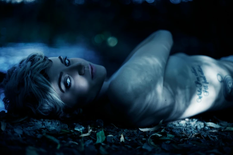 a woman laying on the ground in the dark, an album cover, featured on cgsociety, with blue skin, night in the forest, androgyn beauty, chloe price