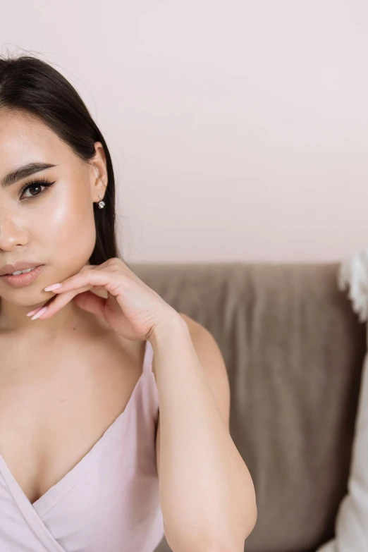 a woman in a pink dress sitting on a couch, inspired by Natasha Tan, trending on pexels, photorealism, asian beautiful face, wearing pearl earrings, skincare, smooth symmetrical chin