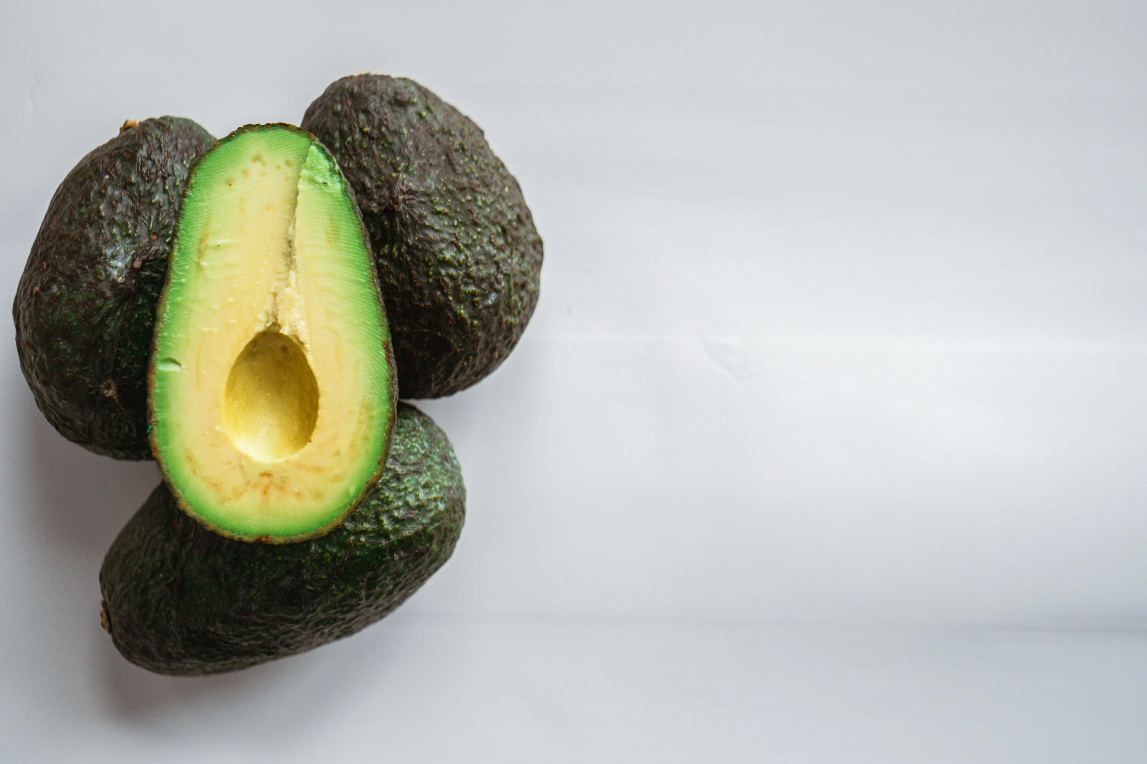 an avocado cut in half on a white surface, pexels, hyperrealism, background image