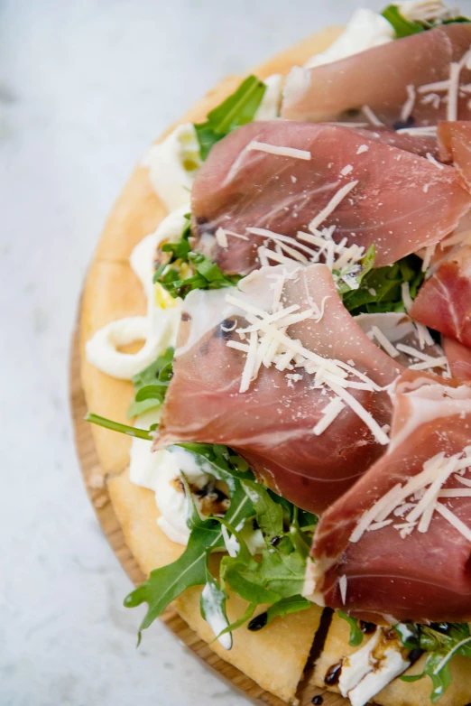 a pizza topped with prosciutto and cheese, caparisons, on a wooden plate, pointè pose, zoomed in