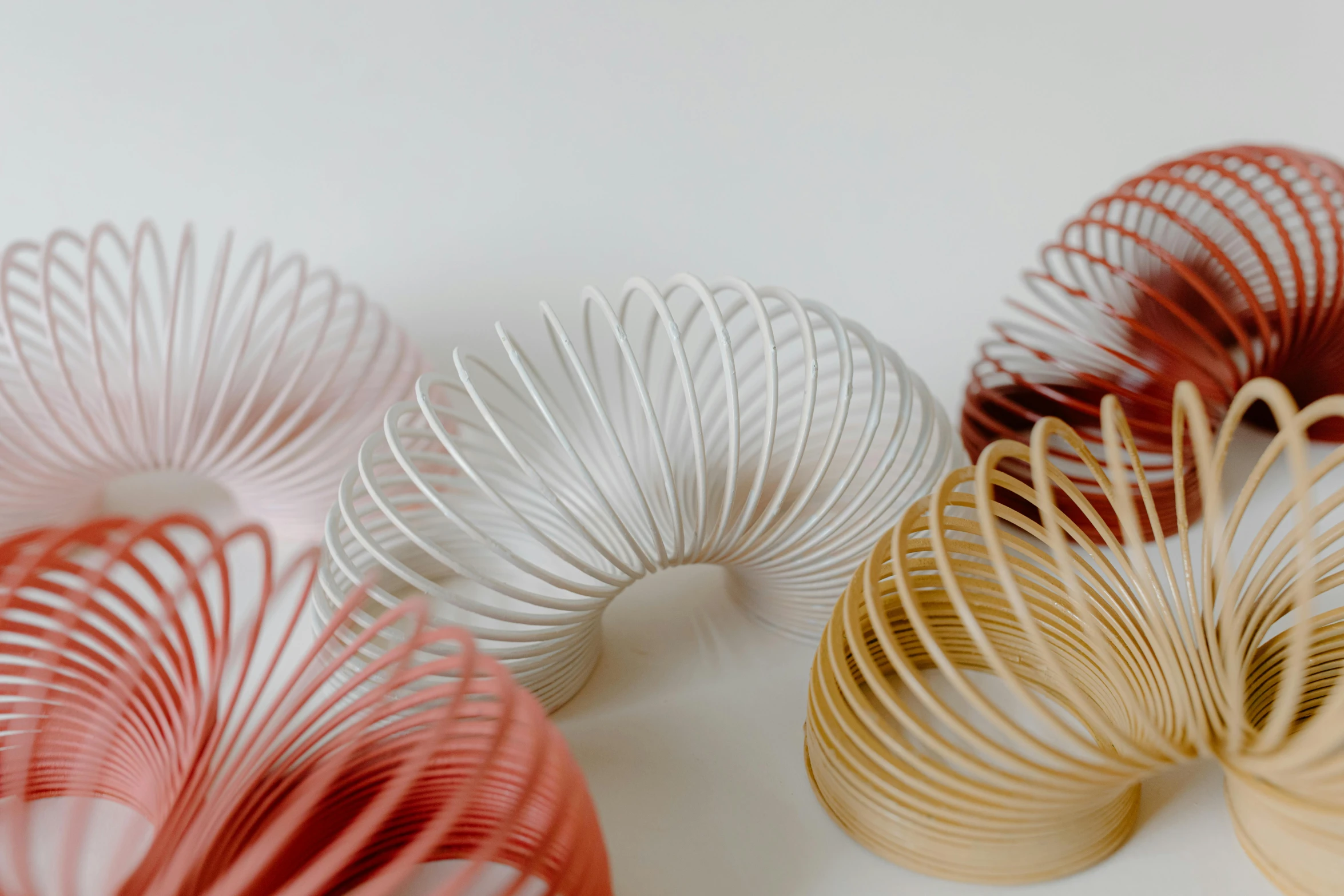 a group of slink toys sitting on top of a table, inspired by Anna Füssli, trending on unsplash, kinetic art, spiral lines, warm coloured, white sweeping arches, close-up product photo