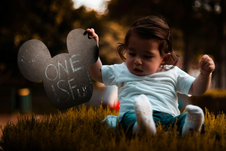 a little girl sitting in the grass holding a sign, pexels contest winner, mickey mouse, with a black background, jose miguel roman frances, thumbnail