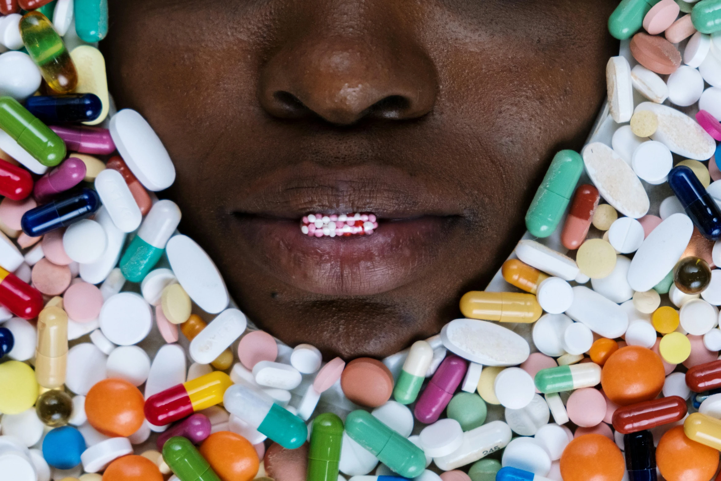 a close up of a person surrounded by pills, an album cover, inspired by Damien Hirst, trending on pexels, hyperrealism, ( ( dark skin ) ), chewing tobacco, contracept, multicolored