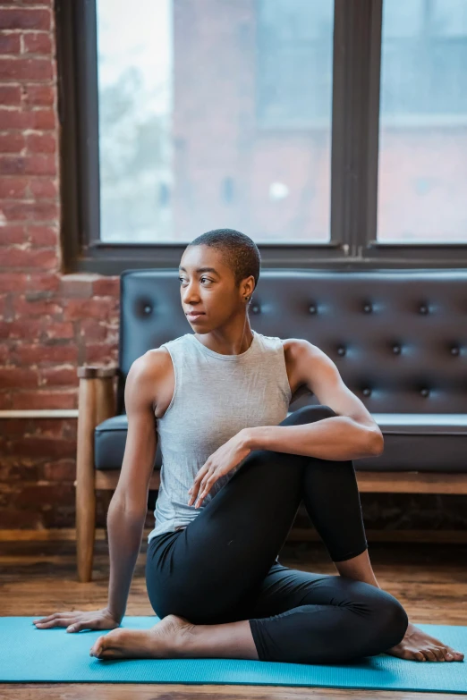 a woman sitting on a yoga mat in front of a window, a portrait, by Lily Delissa Joseph, trending on unsplash, androgynous male, ashteroth, sitting on a mocha-colored table, wearing a muscle tee shirt