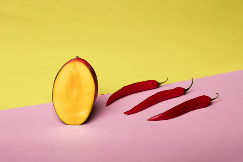 a piece of fruit sitting on top of a pink and yellow surface, inspired by Stanton Macdonald-Wright, trending on pexels, chili, split in half, on grey background, red and yellow light