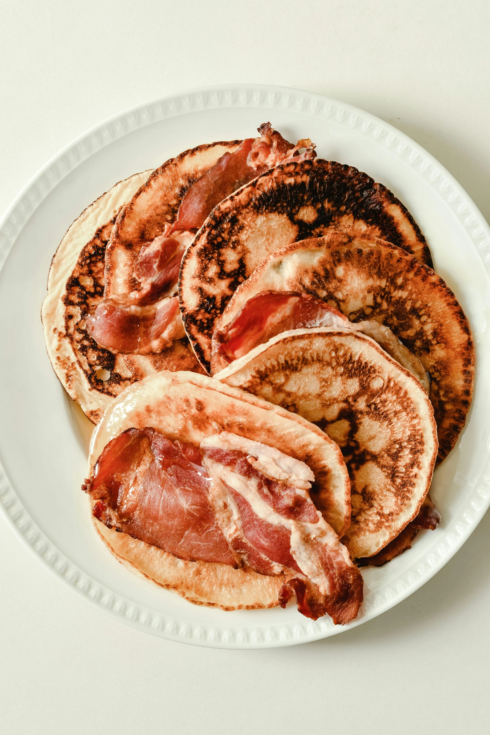 a white plate topped with pancakes covered in bacon, 🦩🪐🐞👩🏻🦳, high angle close up shot, various sizes, aged