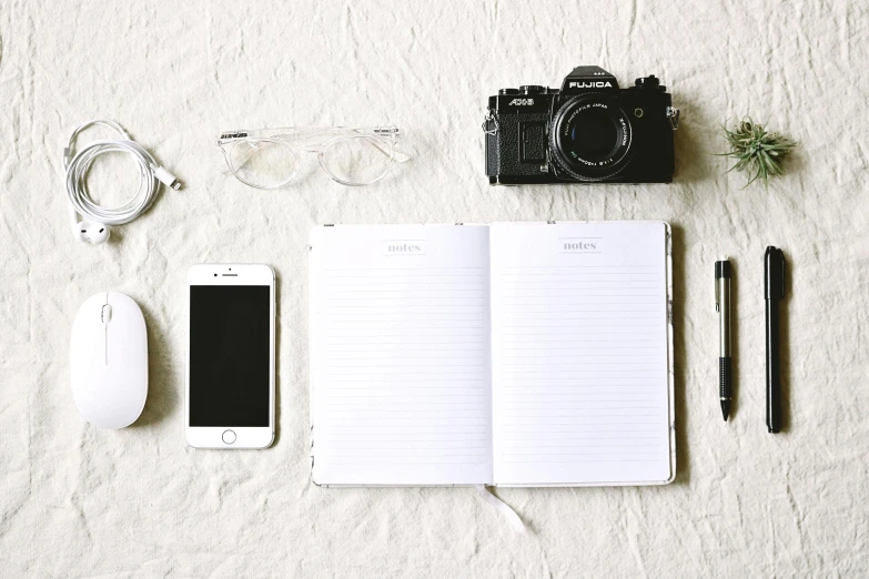 an open notebook sitting on top of a bed next to a camera, a picture, trending on pexels, minimalism, silver accessories, professional iphone photo, white backdrop, various posed