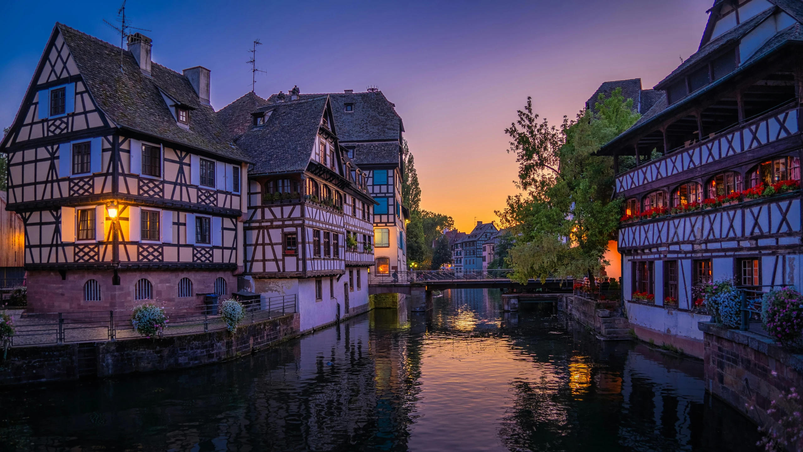 a river running through a small town next to tall buildings, pexels contest winner, renaissance, evening lanterns, french village exterior, soft glow, pink