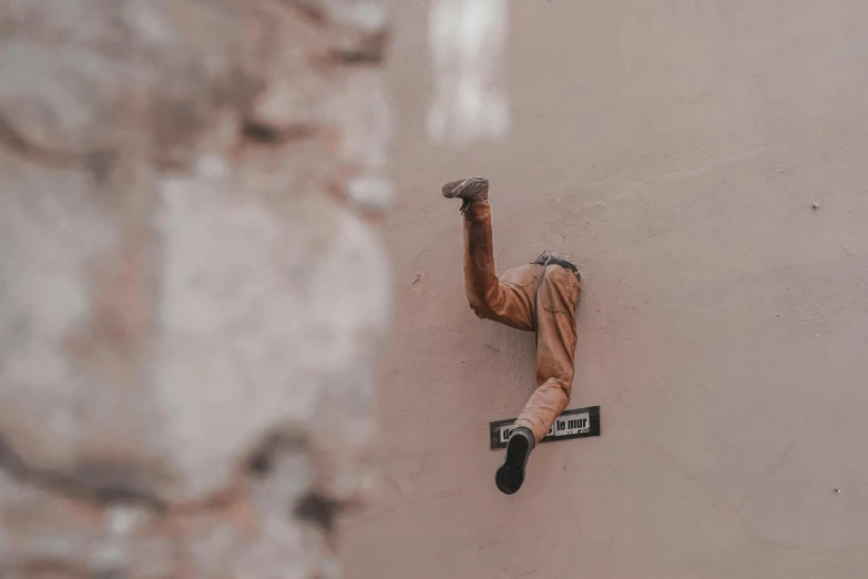 a man hanging on to the side of a building, a statue, inspired by Jeremy Geddes, pexels contest winner, street art, action figurine toy, light - brown wall, ((rust)), waving