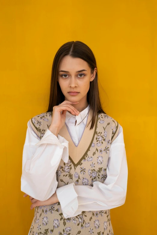 a woman standing in front of a yellow wall, trending on unsplash, renaissance, wearing a vest and a tie, frown fashion model, wearing a white sweater, flowery