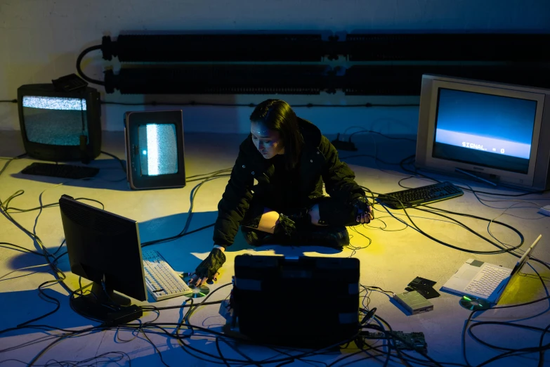 a woman sitting on the floor working on a laptop, inspired by Elsa Bleda, computer art, cables and monitors, like a cyberpunk workshop, stacked computer screens, performance