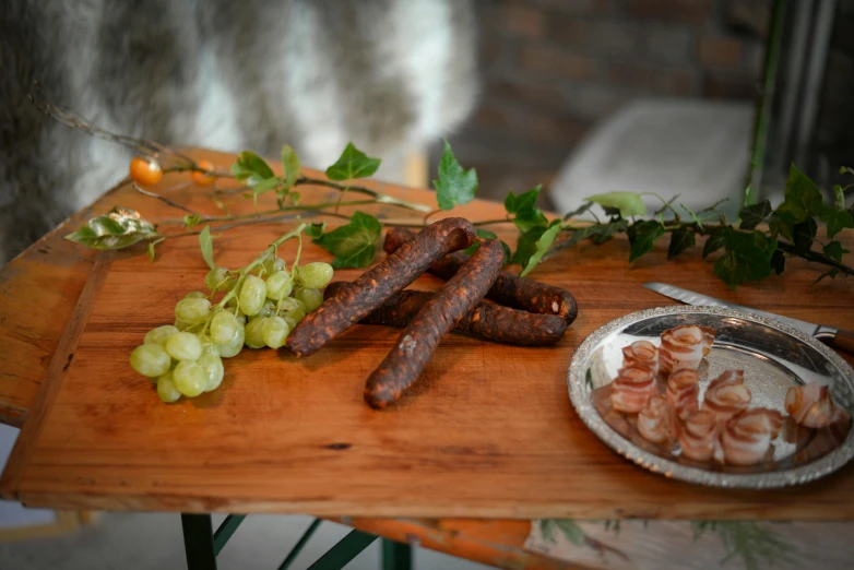 a cutting board with sausages and grapes on it, by Emma Andijewska, pexels contest winner, private press, festive atmosphere, twigs, angled shot, medium long shot