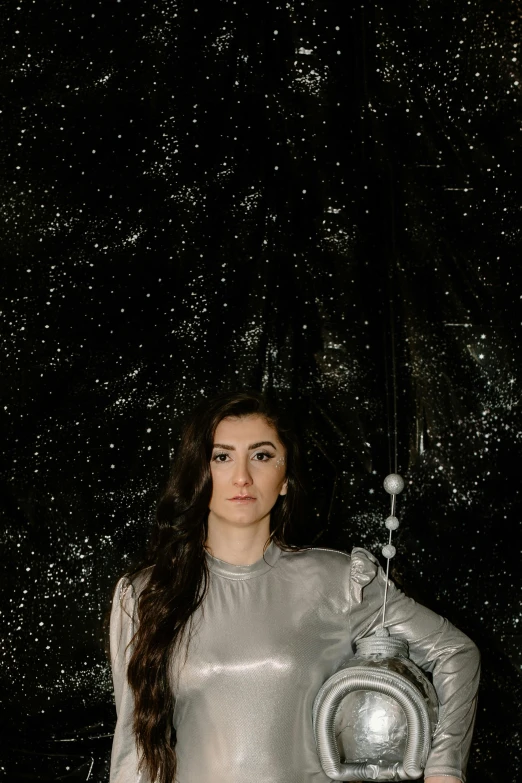 a woman in a shiny silver outfit posing for a picture, an album cover, inspired by Ion Andreescu, unsplash, light and space, dressed in stars and planets, portrait photo of a backdrop, elizabeth saltzman, taken in the late 2010s