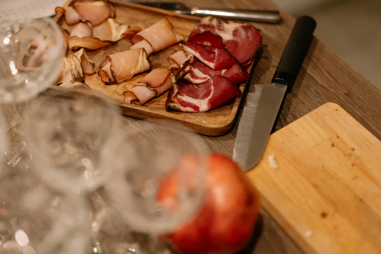 a cutting board sitting on top of a wooden table, by Niko Henrichon, pexels contest winner, renaissance, ham, drinking, fresh kill, close to night