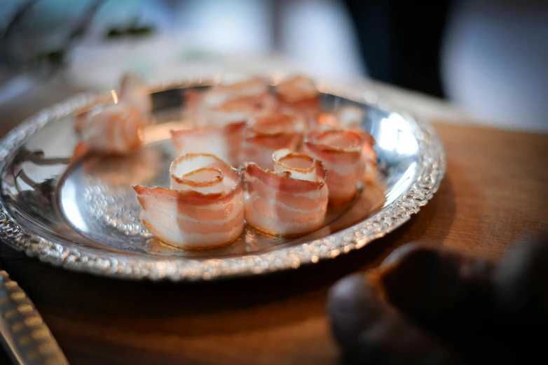 a plate of bacon wrapped in bacon sitting on a table, by Sylvia Wishart, pexels, shrimp, silver platter, kek, bells