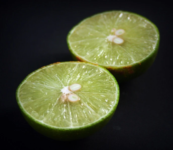 two limes cut in half on a black surface, a macro photograph, pexels, close up of iwakura lain, close - up photo, close-up photo, close up iwakura lain