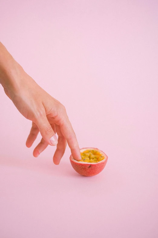 a person reaching for a piece of fruit, pink and yellow, hand model, jen atkin, passion fruits