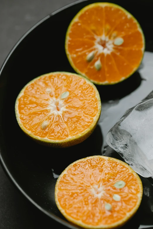 a black plate topped with sliced oranges on top of a table, ice cubes, organics, multiple stories, 6 pack