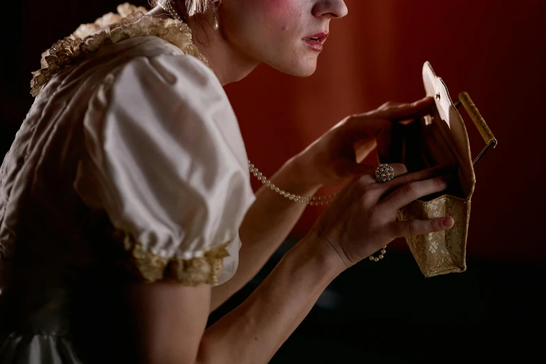 a woman looking in a mirror while holding a purse, inspired by Georges de La Tour, trending on pexels, magic realism, theatre equipment, julia garner, real pearls, thick dust and red tones