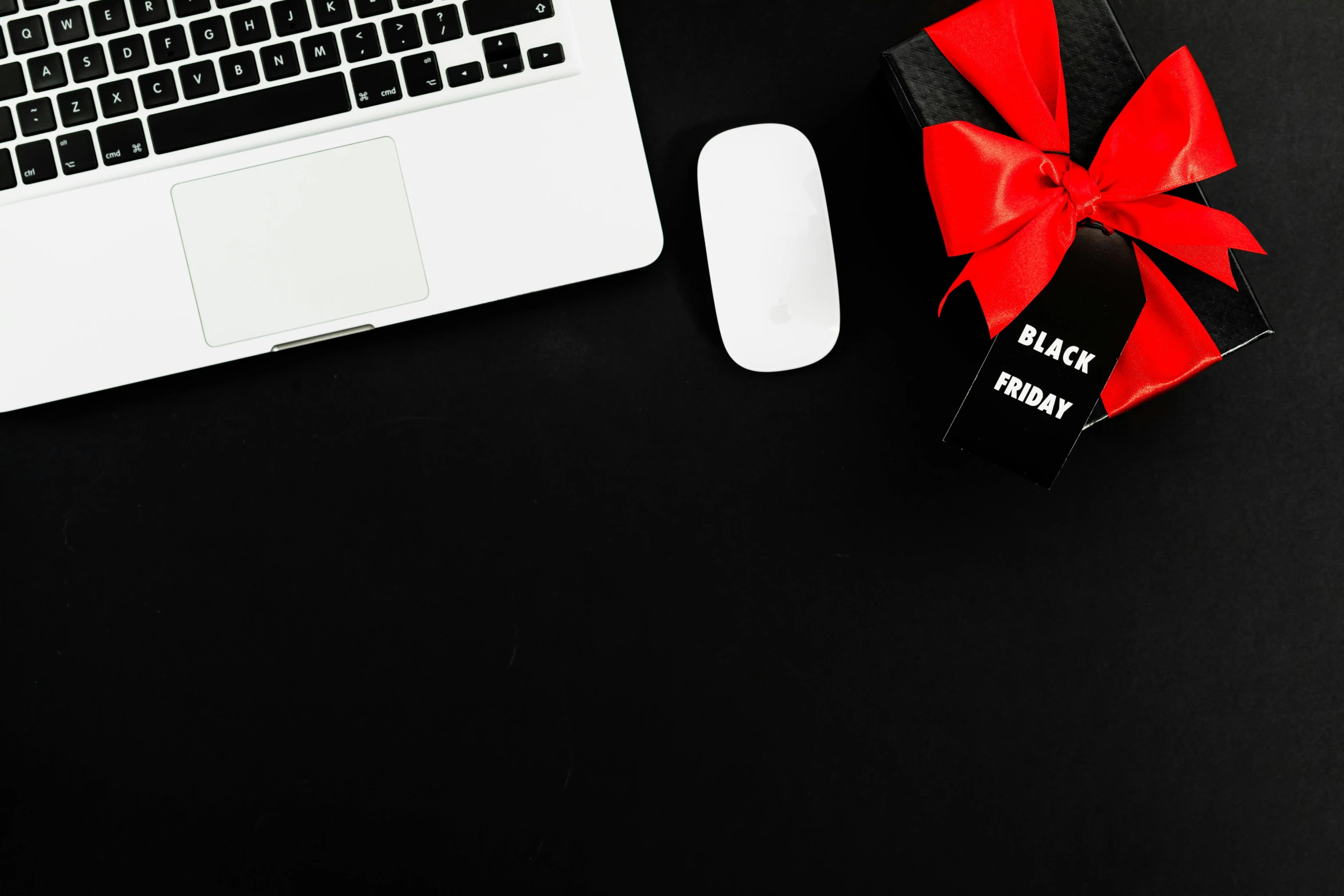 a laptop computer sitting on top of a desk next to a red bow, a black and white photo, pexels contest winner, black flat background, background image, wearing festive clothing, all black matte product