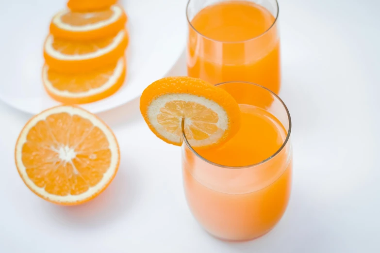 a couple of glasses filled with orange juice, pexels, hurufiyya, on a white table, instagram post, grey orange, monkey punch