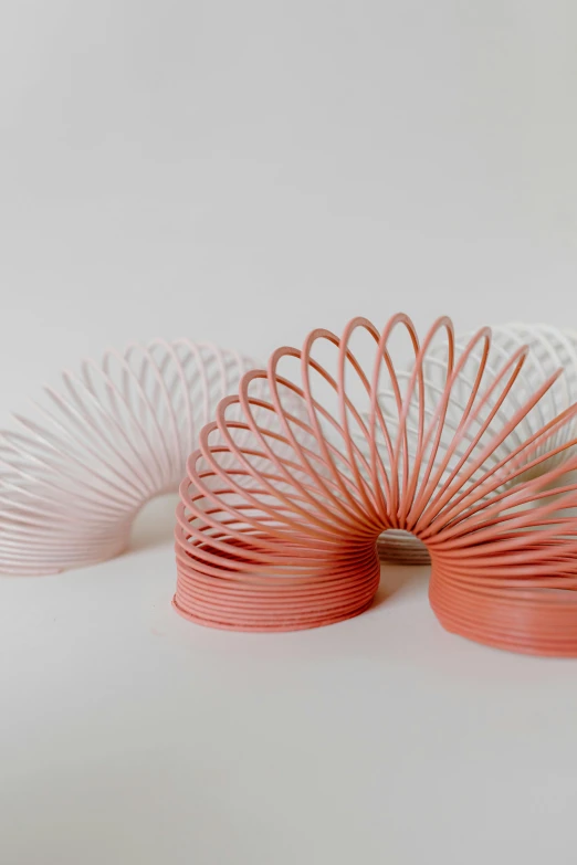 a pink slink toy sitting on top of a white surface, by jeonseok lee, trending on unsplash, kinetic art, intricate spirals, orange and white, a pair of ribbed, made of wire