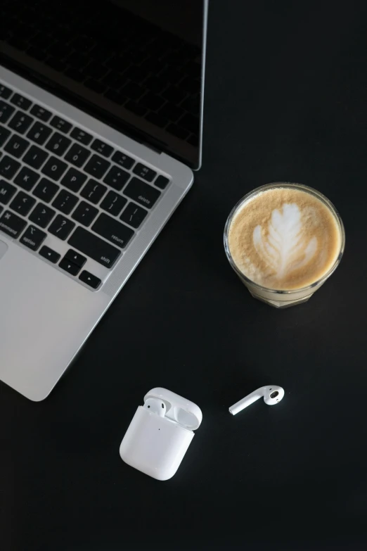 a laptop computer sitting on top of a desk next to a cup of coffee, by Andries Stock, trending on pexels, airpods, white on black, latte art, no - text no - logo